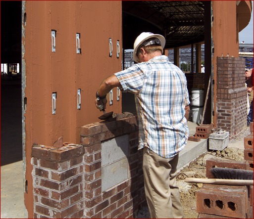 A mason lays brick over a Densglass structural wall coated with a red, fluid-applied air and water barrier. Mason contractors are discovering the benefits of installing air barriers themselves, rather than subbing it out.